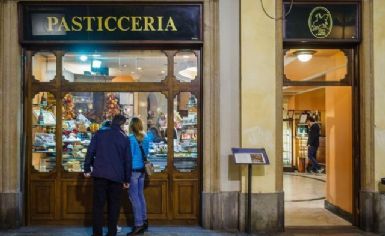 Foto della vetrina di una pasticceria dall'esterno con due persone di spalle che guardano dentro la vetrina