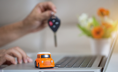 Primo piano di un notebook inquadrato lateralmente, con delle mani sulla tastiera, una delle quali sorregge la chiave di un'automobile