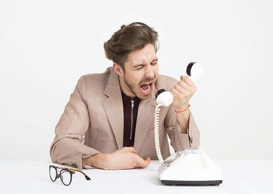 Foto di un uomo che strilla dentro la cornetta di un telefono a filo.