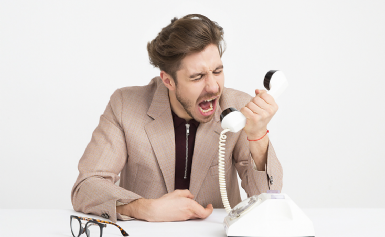 Foto di un uomo che strilla dentro la cornetta di un telefono a filo.